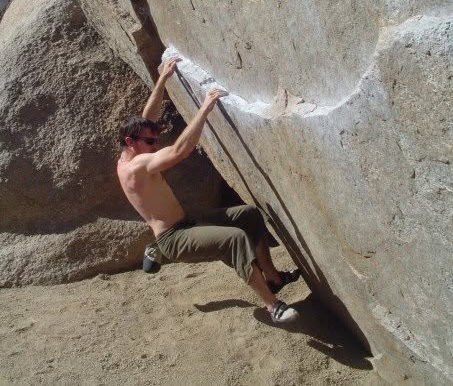 Climber working a technical boulder problem on granite