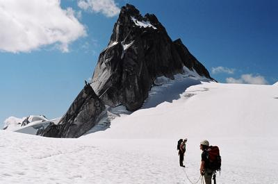 Two alpinists on a snowfield below a dramatic granite spire