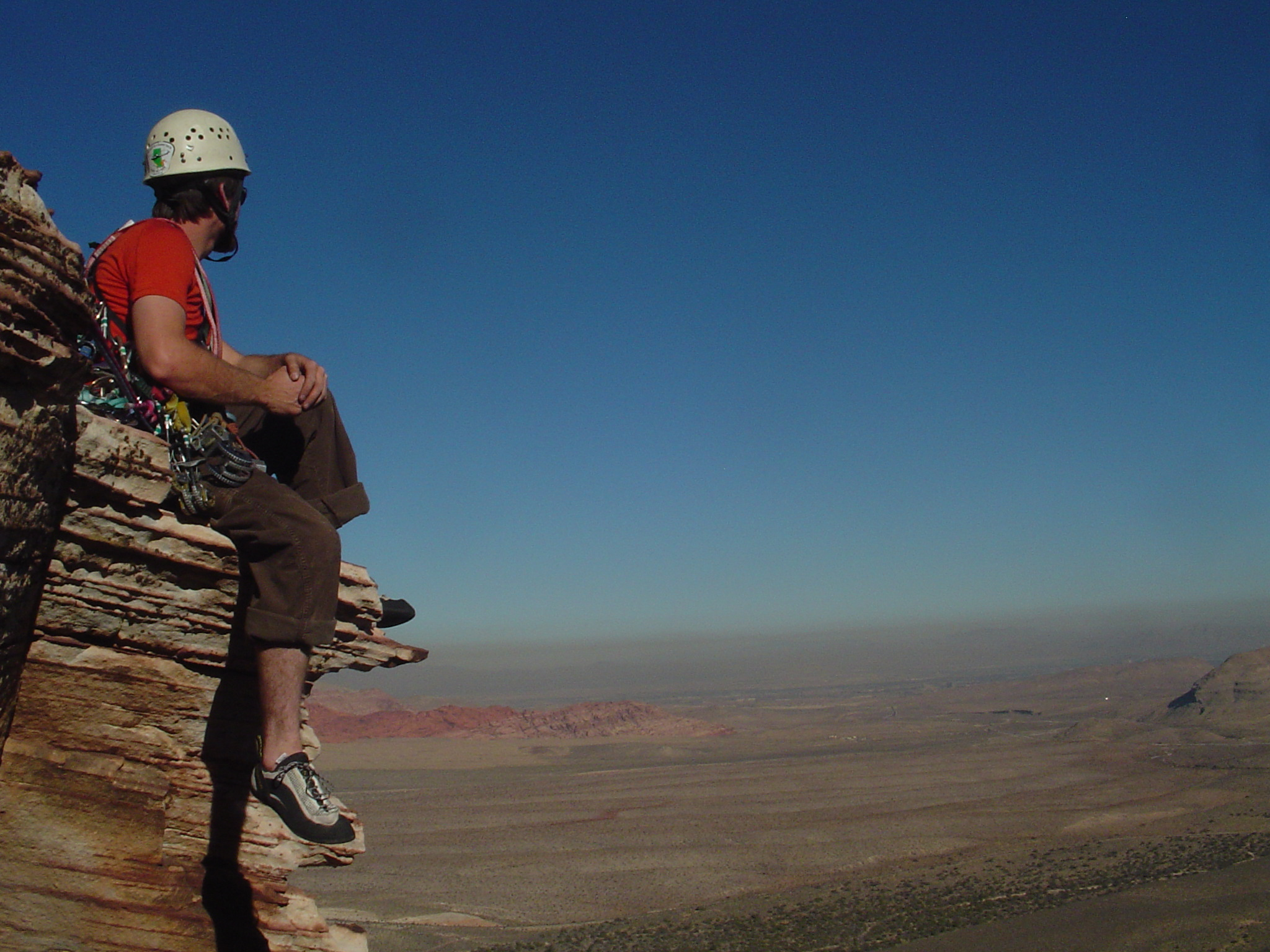 Jon sitting on a ledge at Red Rocks, Nevada, gear racked and gazing out over the desert