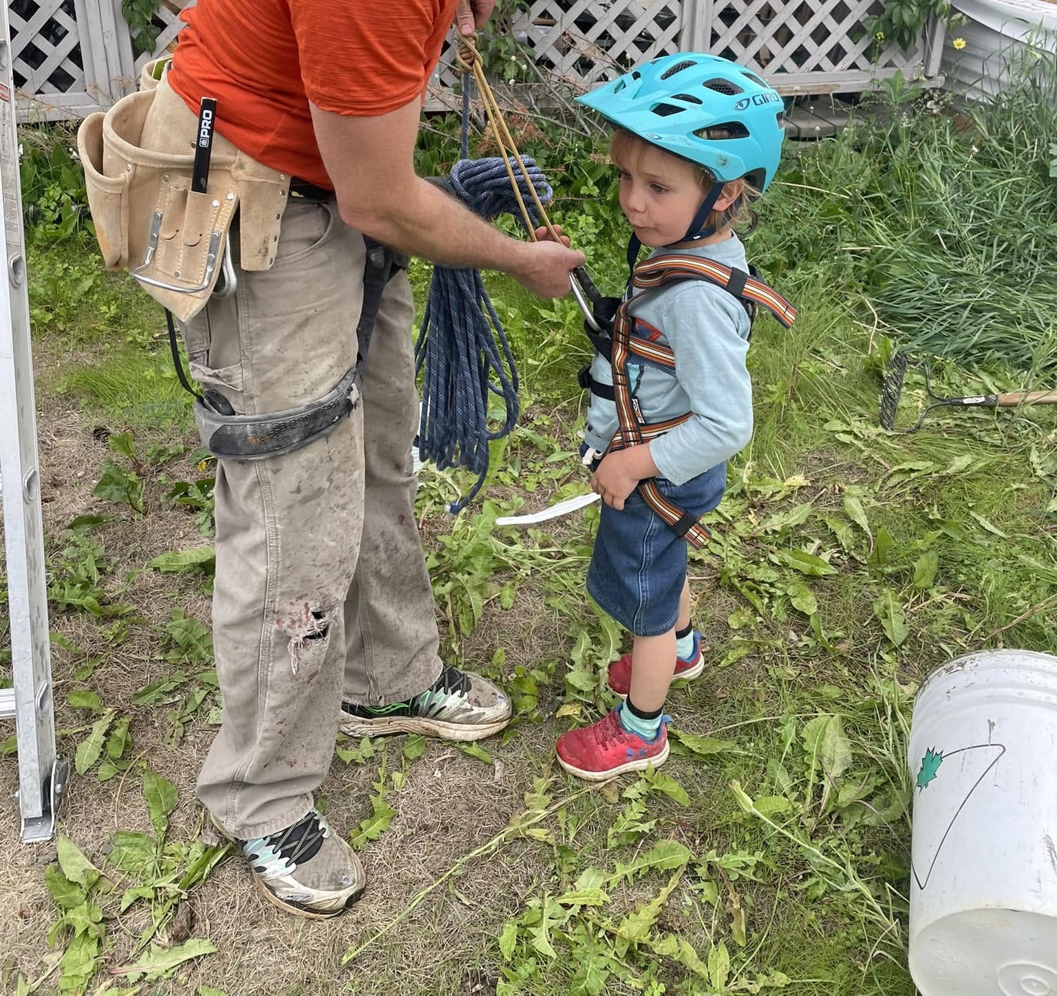 A parent carefully fitting a climbing harness on a young toddler in a helmet