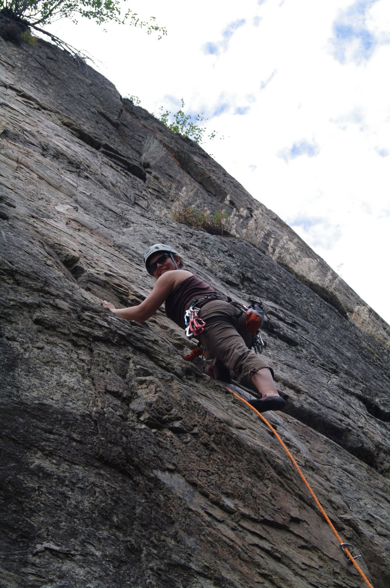 Rudie relaxed at a belay station, smiling, mountains behind