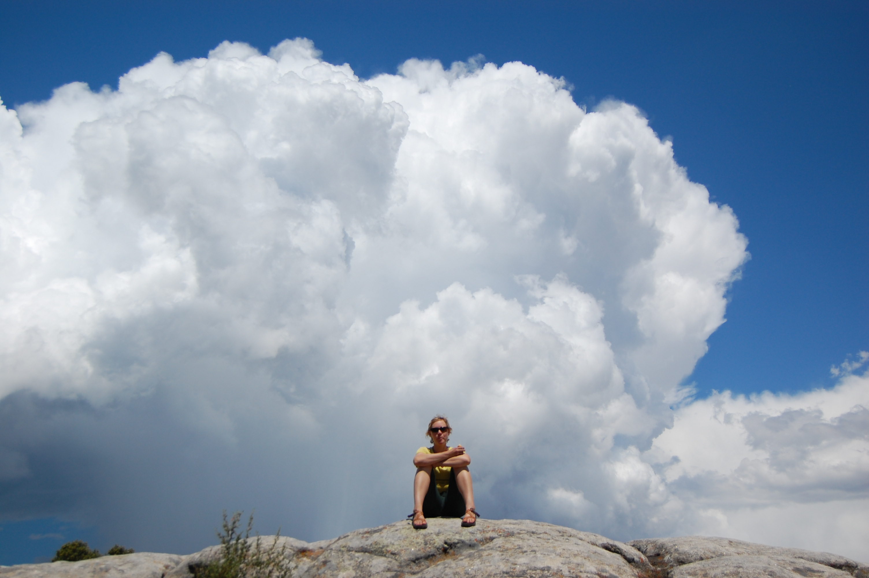 Rudie sitting on a granite dome, dwarfed by a massive cumulus cloud rising behind her